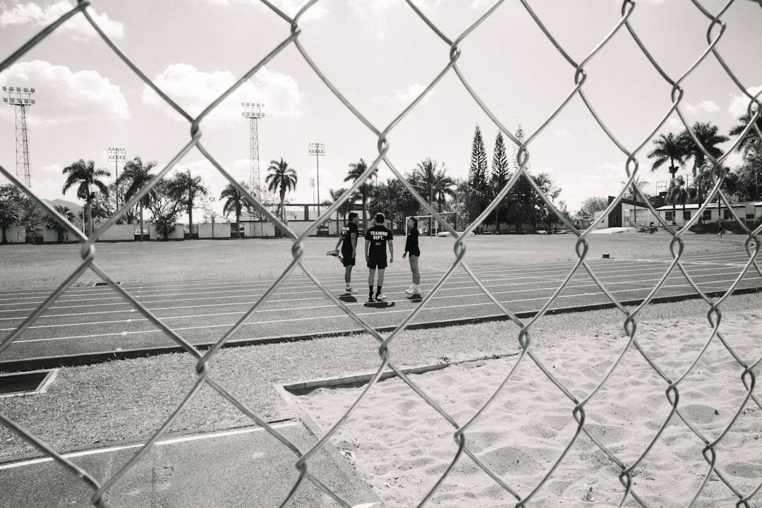 three-people-stand-on-a-running-track-behind-a-fence-uelklqud13o